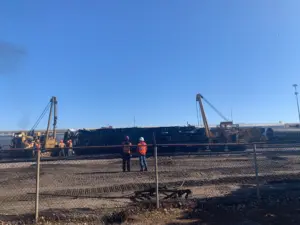 Two recovery sidebooms lifting a derailed locomotive during a railroad recovery equipment operation at a rail yard