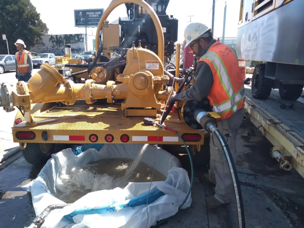Worker operating a trailer-mounted hydrostatic fill and test unit, filling a pipeline test section with water on a jobsite