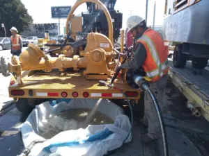 Worker operating a trailer-mounted hydrostatic fill and test unit, filling a pipeline test section with water on a jobsite