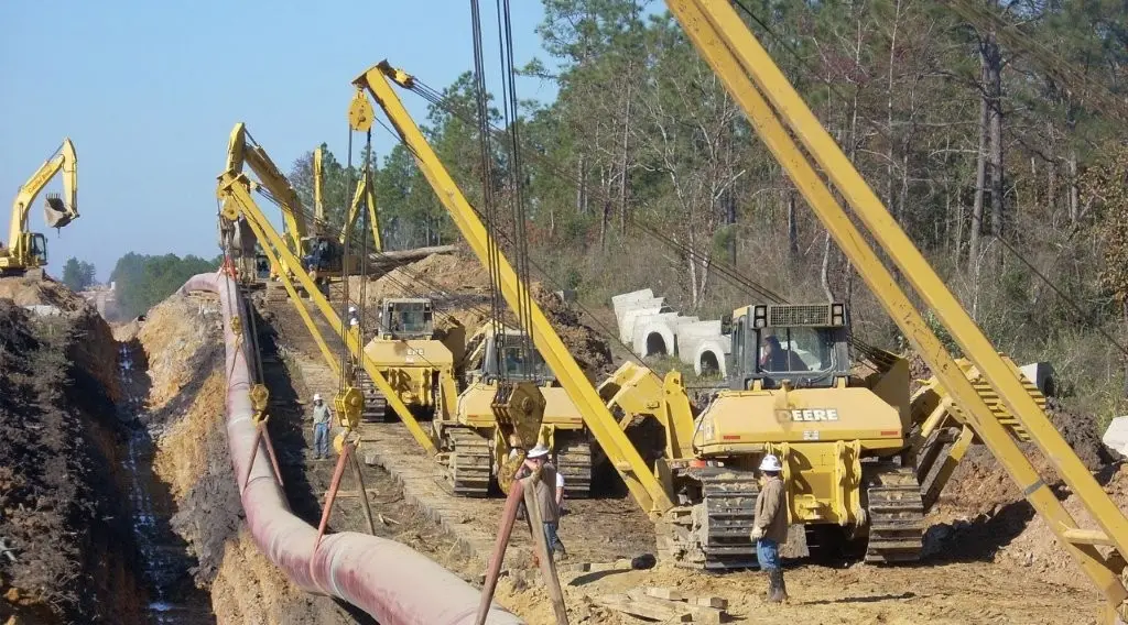 Pipeline lowering-in operation with a coordinated row of sideboom pipelayers lowering a coated welded pipe string into the trench along the right-of-way.