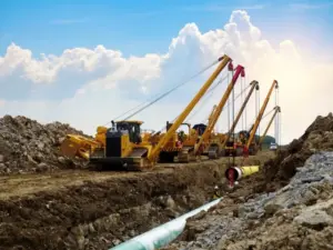 Pipeline right-of-way construction with sideboom tractors lowering steel pipe into a trench at a Midwestern Manufacturing jobsite.