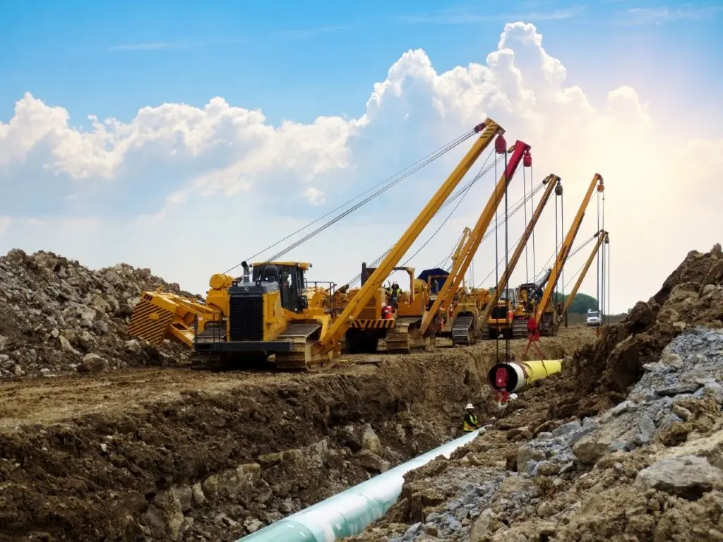 Pipeline right-of-way construction with sideboom tractors lowering steel pipe into a trench at a Midwestern Manufacturing jobsite.